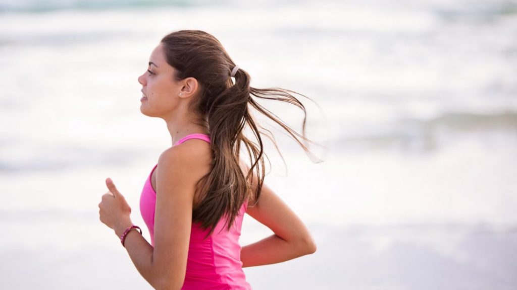 Side view of a young woman jogging on a beach wearing pink active wear.