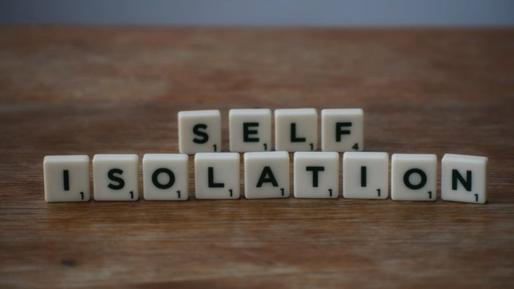 Scrabble tiles spelling 'self isolation' on a wooden surface, symbolizing solitude.
